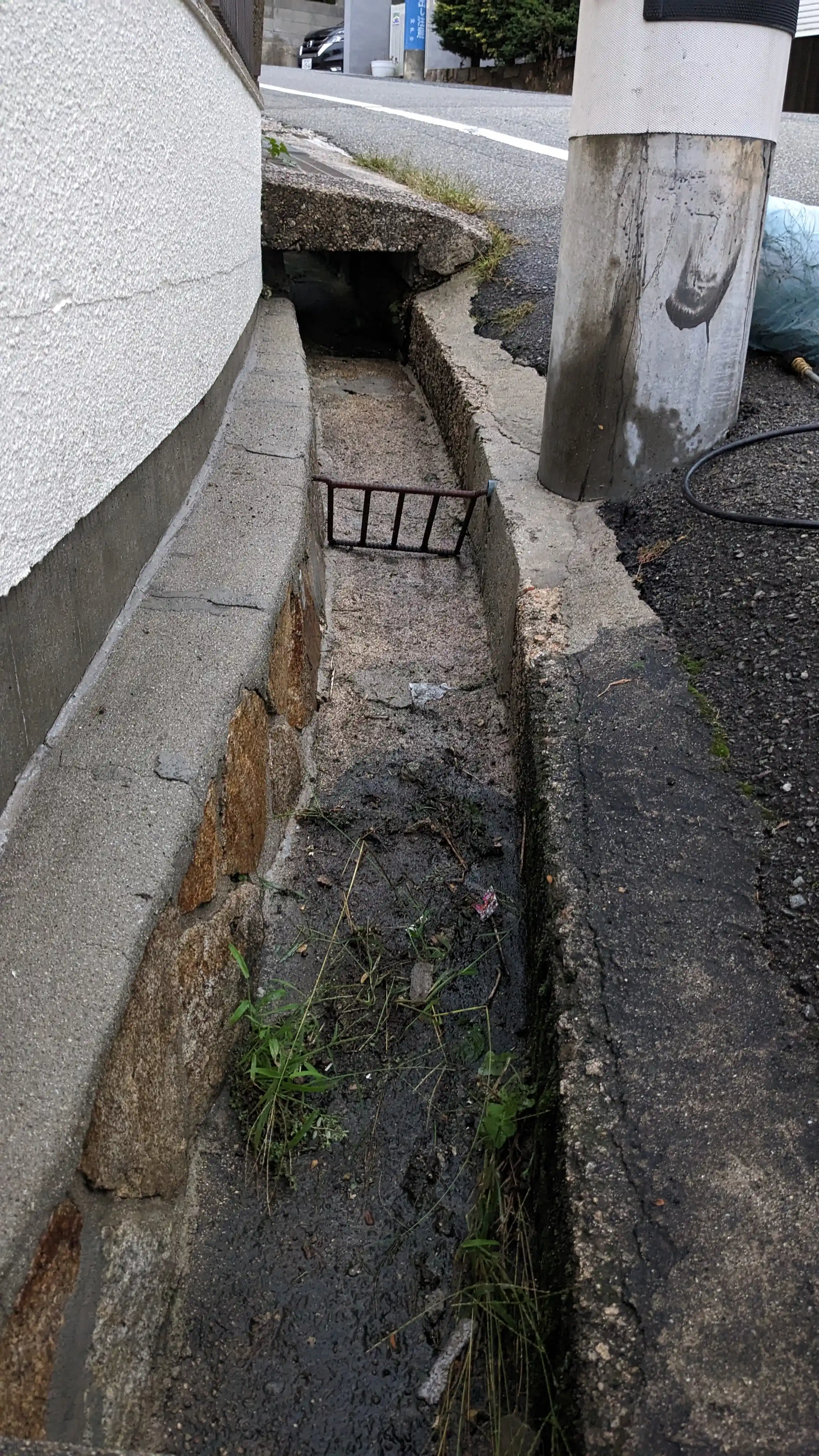 Roadside concrete drain channel cleaned along a Japanese house exterior